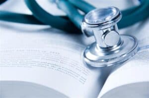 A teal stethoscope resting on an open page of a medical textbook, representing scholarly medical education and research