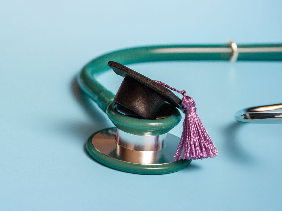 A stethoscope laid down with a miniature graduation convocation cap on top of it.