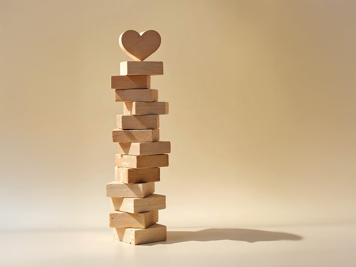 A stack of wooden blocks resembling Jenga blocks with a wooden heart shape at the very top.