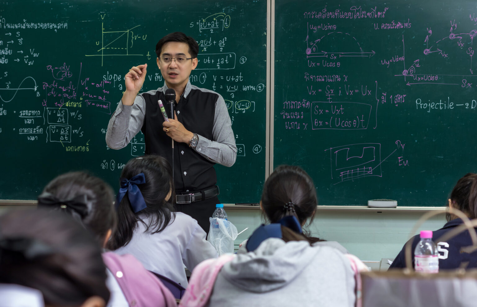 Asian teacher Giving Lesson to group of College Students which answer the question in the classroom over the physics formular in thai laguage on black board, school education concept