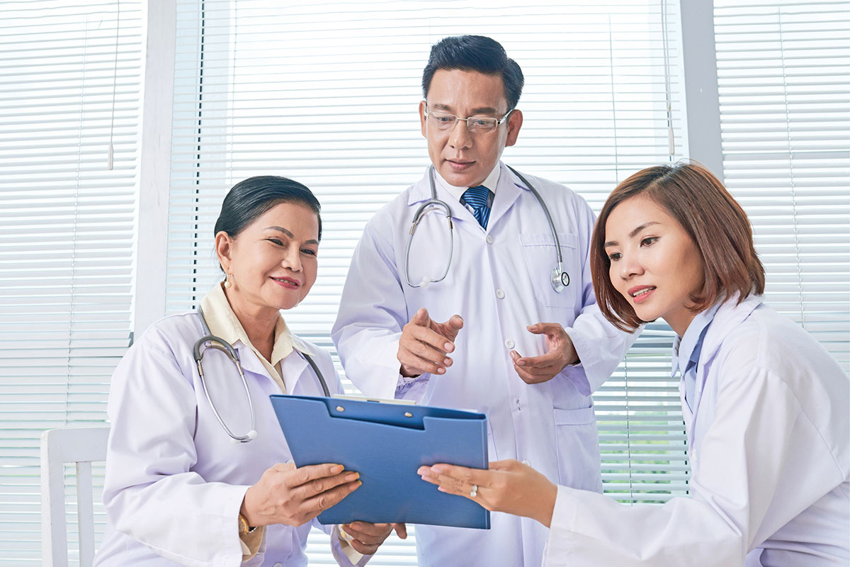 A male doctor and two female doctors look at a paperboard facing the front curiously.