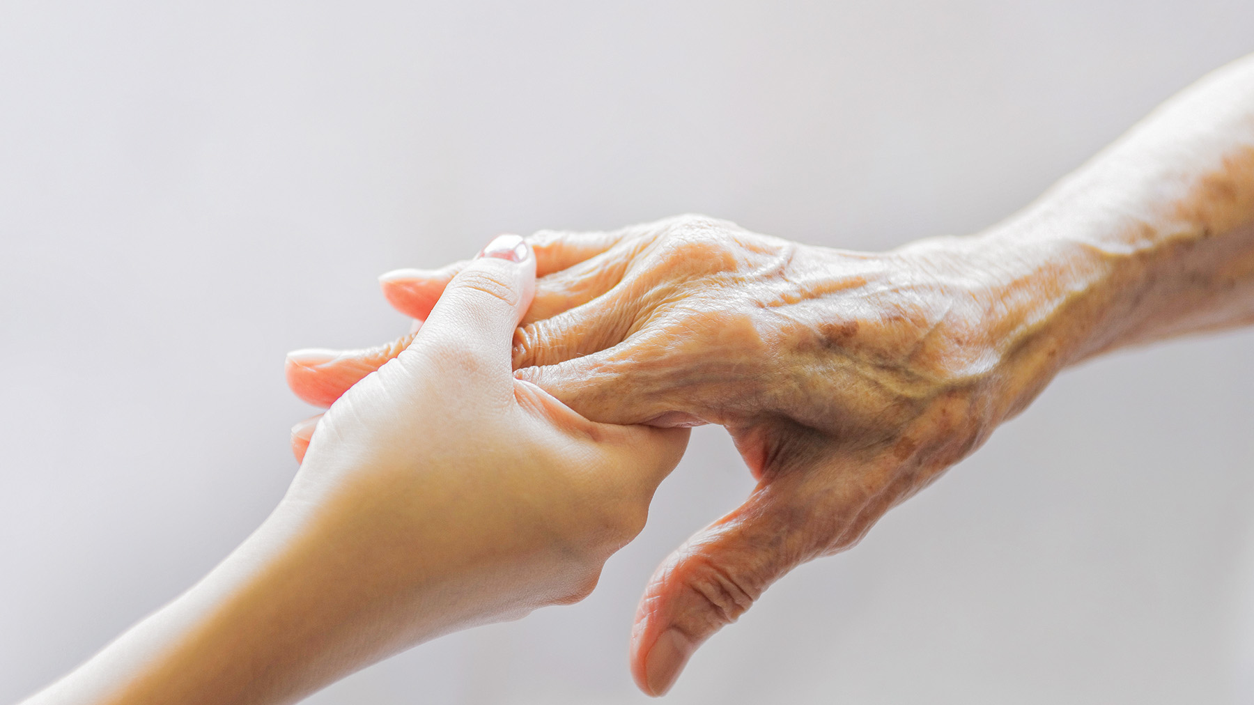 An arm from a young person grabs onto an arm from an elderly person.