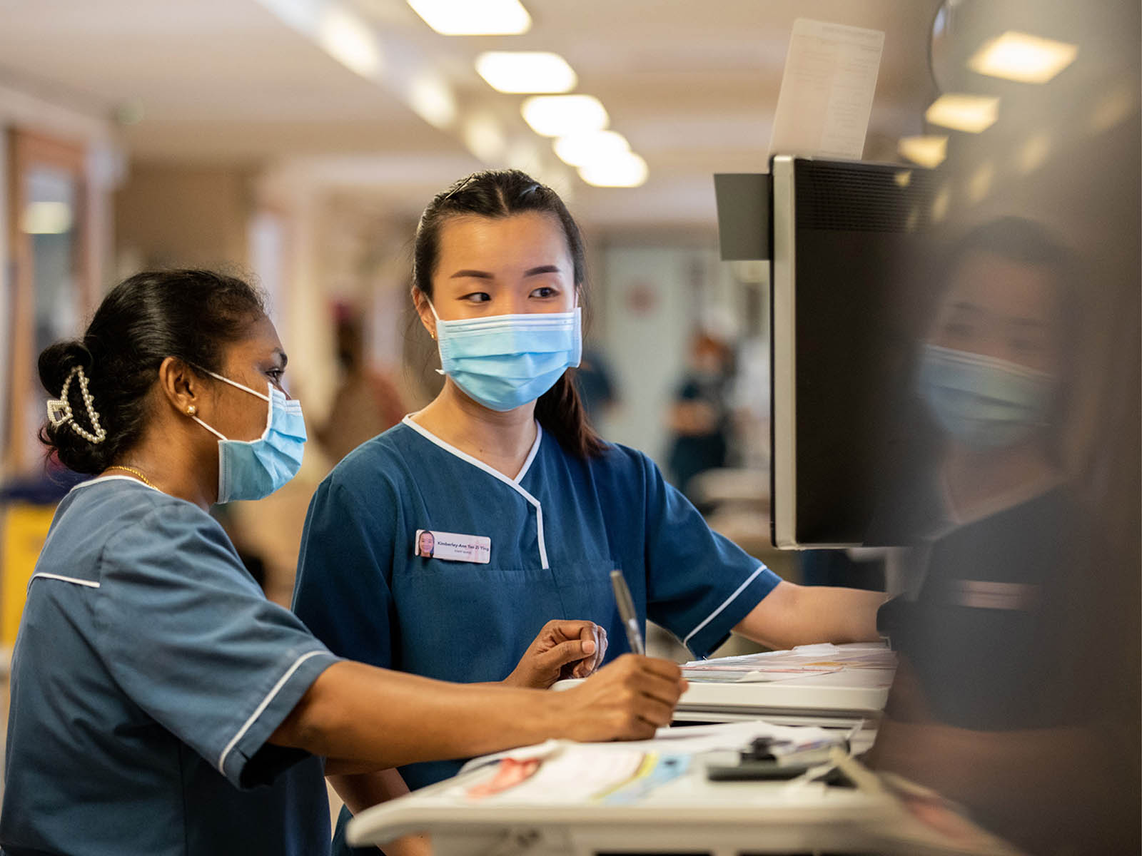 Photo of Kimberley-Ann Tan Zi Ying (right) speaking to her colleague in one of the wards at Tan Tock Seng Hospital on July 28, 2023.