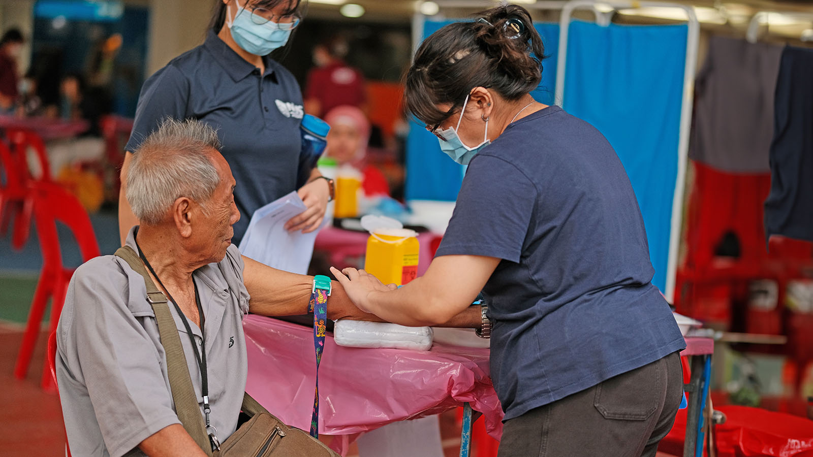 An elderly resident accompanied by a volunteer, to have his blood taken at the phlebotomy station during NHS 2023.