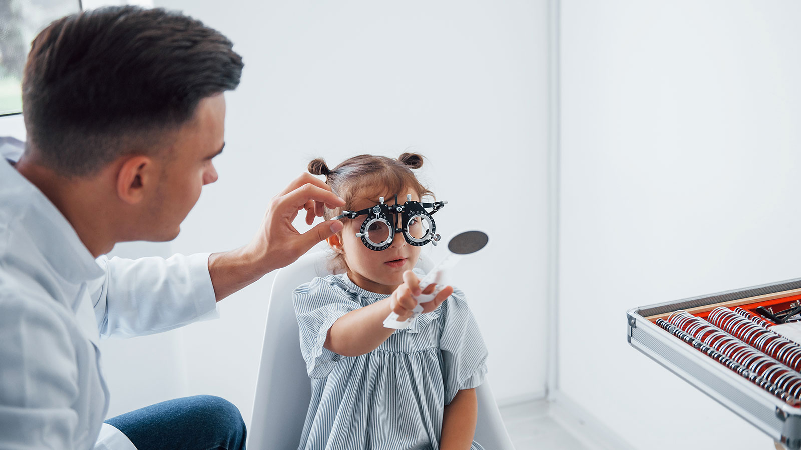 Photo of a male optician helping a young girl test her eyesight through different lenses.