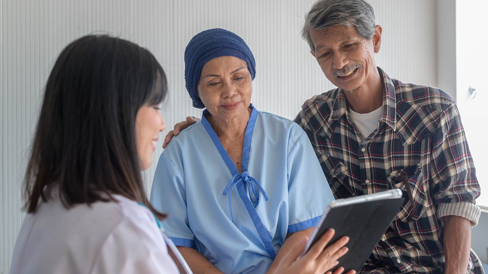 Photo of a female nurse talking to a Muslim female patient and elderly man in a shirt.