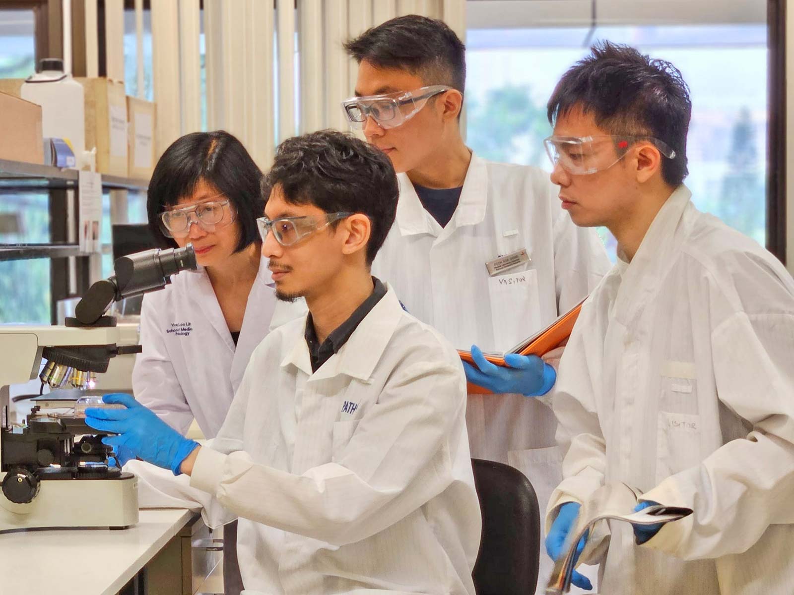 Research team members from Asst Prof Leong Sai Mun’s lab, examining the cell culture plates with co-culture experiment, which led to the discovery of cancer cell altruism. (From left to right: Dr Tan Yuen Peng, Dr Muhammad Sufyan, PhD student Poon Kok Siong, Dr Leong Sai Mun)