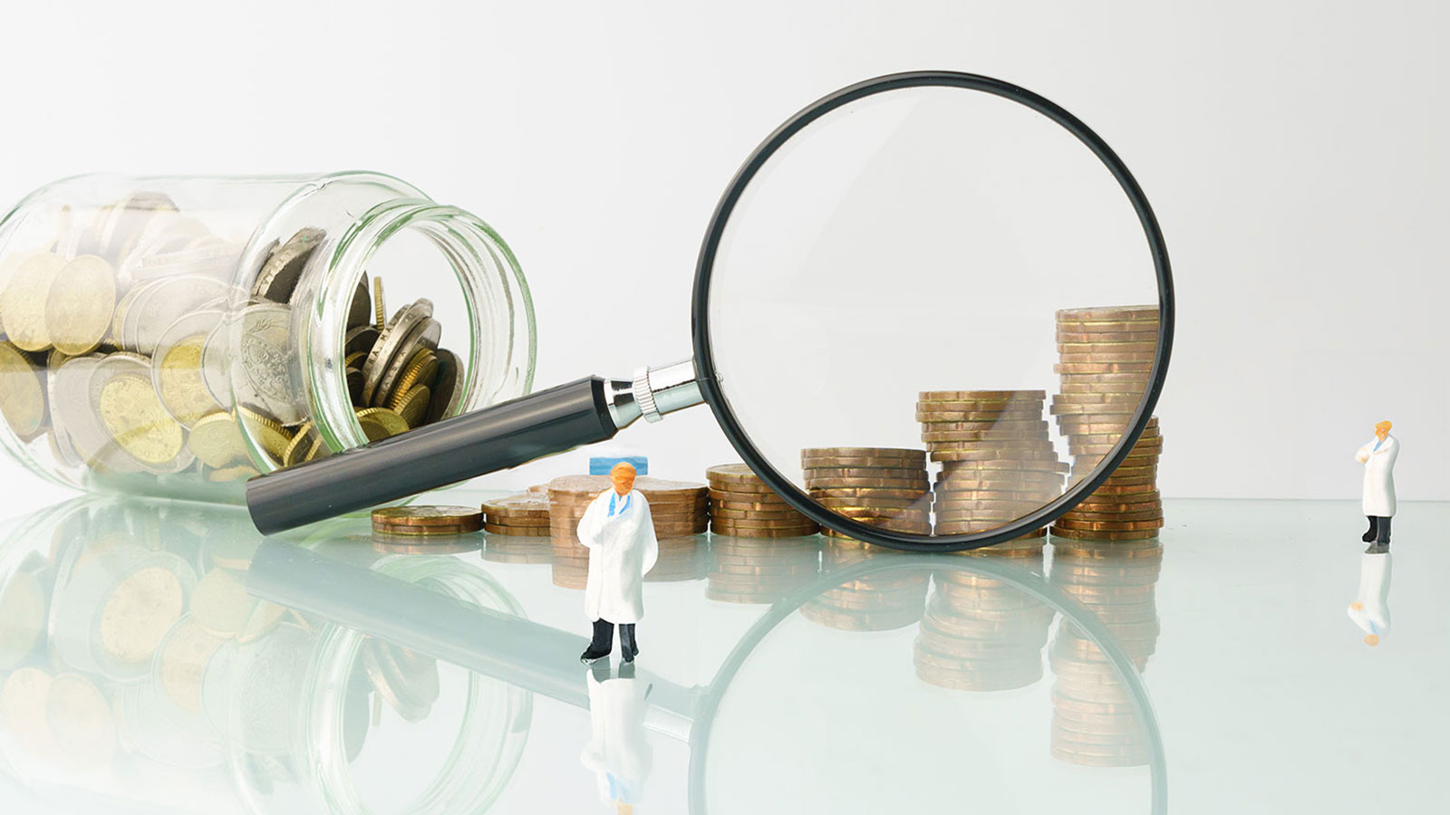 Abstract image of two doctor figuirines standing along a glass jar of coins laid down.