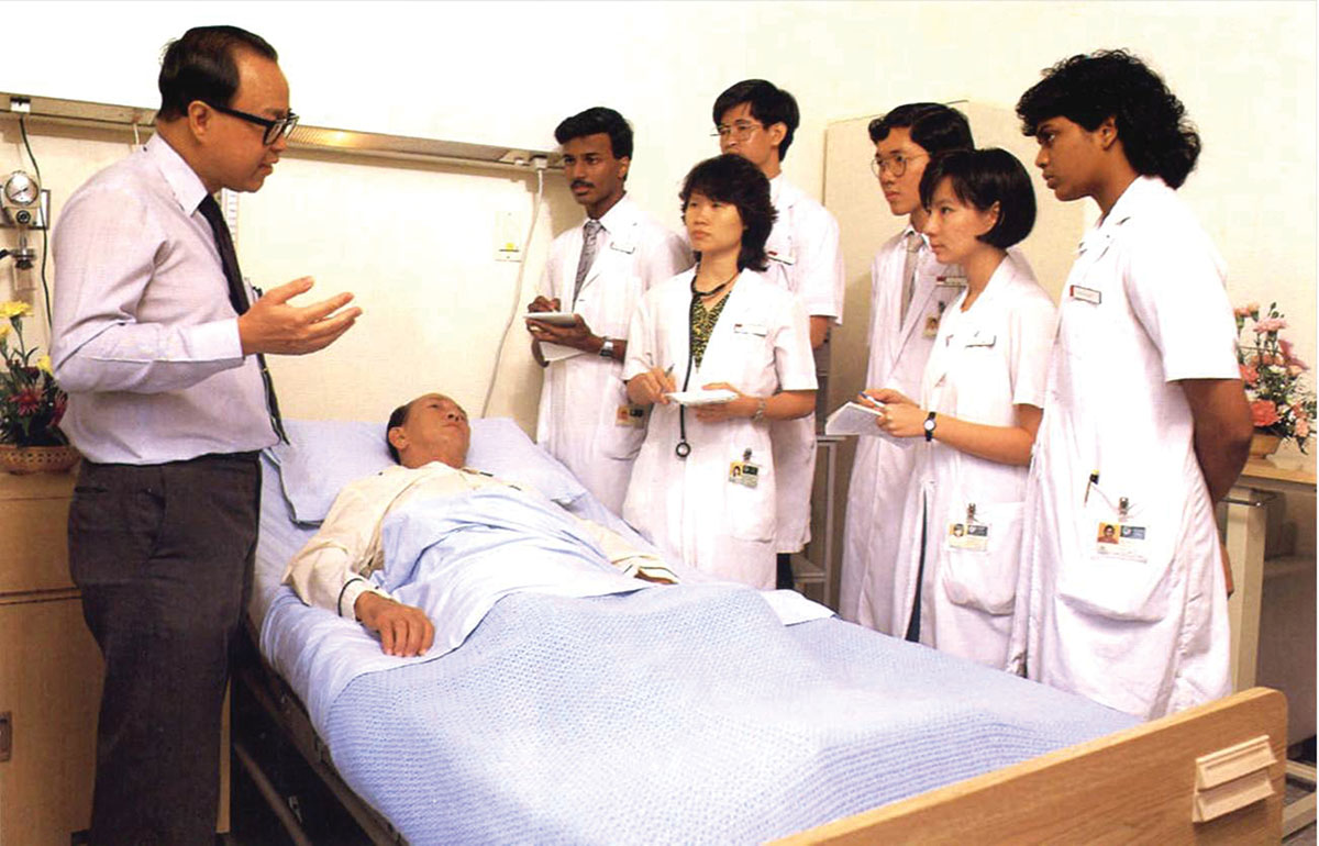 Professor Chia Boon Lock lecturing a group of medical staff trainees, with a patient lying on bed looking towards them.