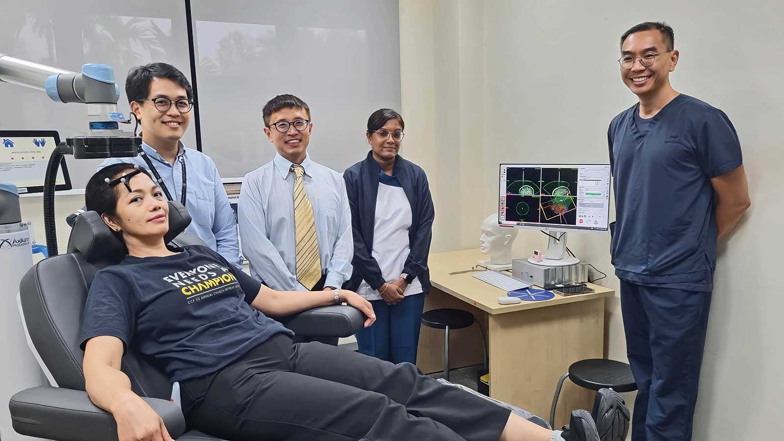 A female patient sits on a dentist chair, with three doctors standing to her left (left-centre of photo), and a doctor standing on the right side of the photo.