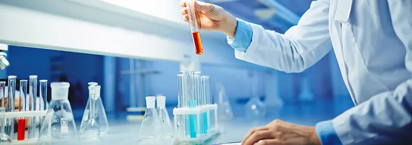 Researcher in a lab holding a test tube with orange liquid working on the latest research news