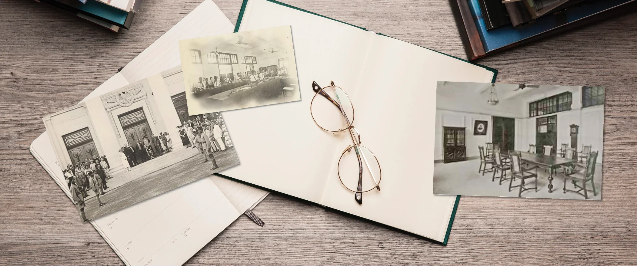 3 monochromatic photos, 2 open empty books, a pair of glasses on top of a wooden table.