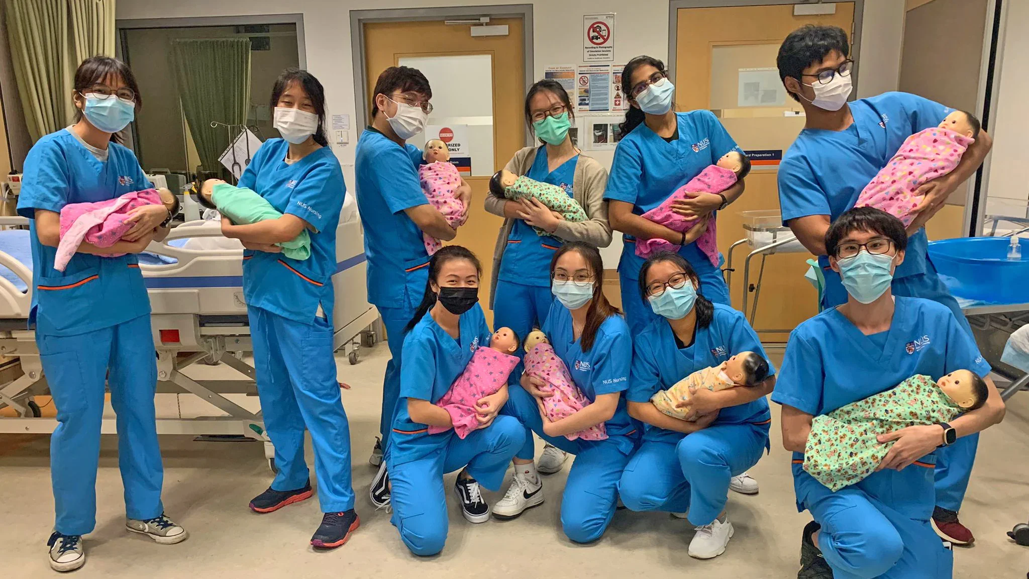 Various nurses in-training carrying infant model units wrapped in teal or pink cloth.